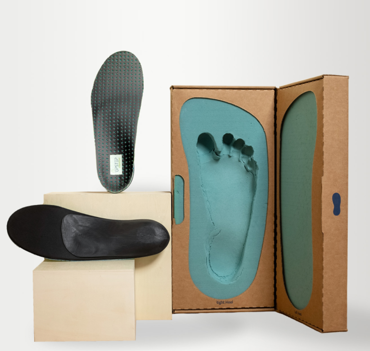 Black custom orthotics placed on two pedestals next to a  custom foot mold 