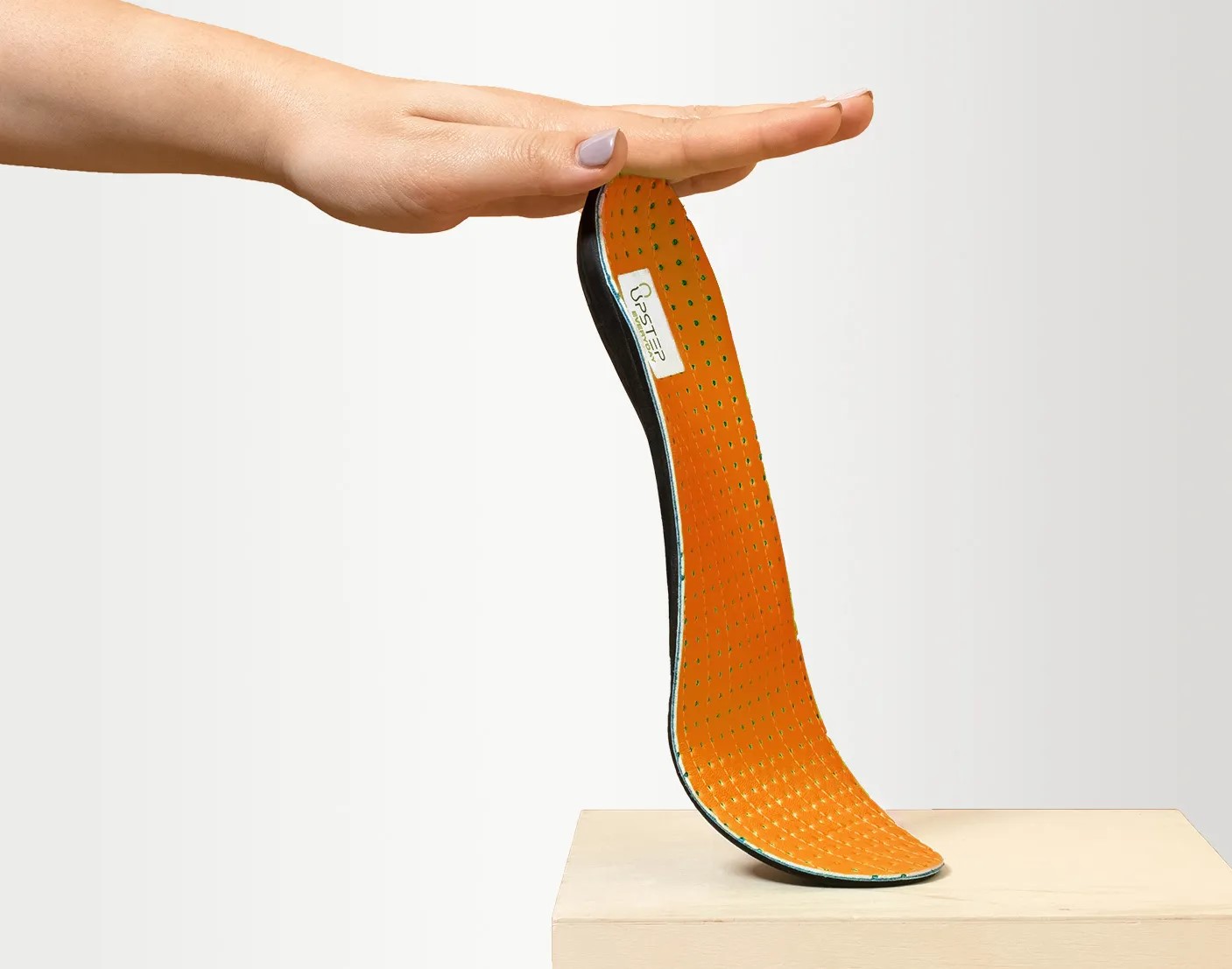 A hand holding the top of an Upstep insole in orange to display it vertically