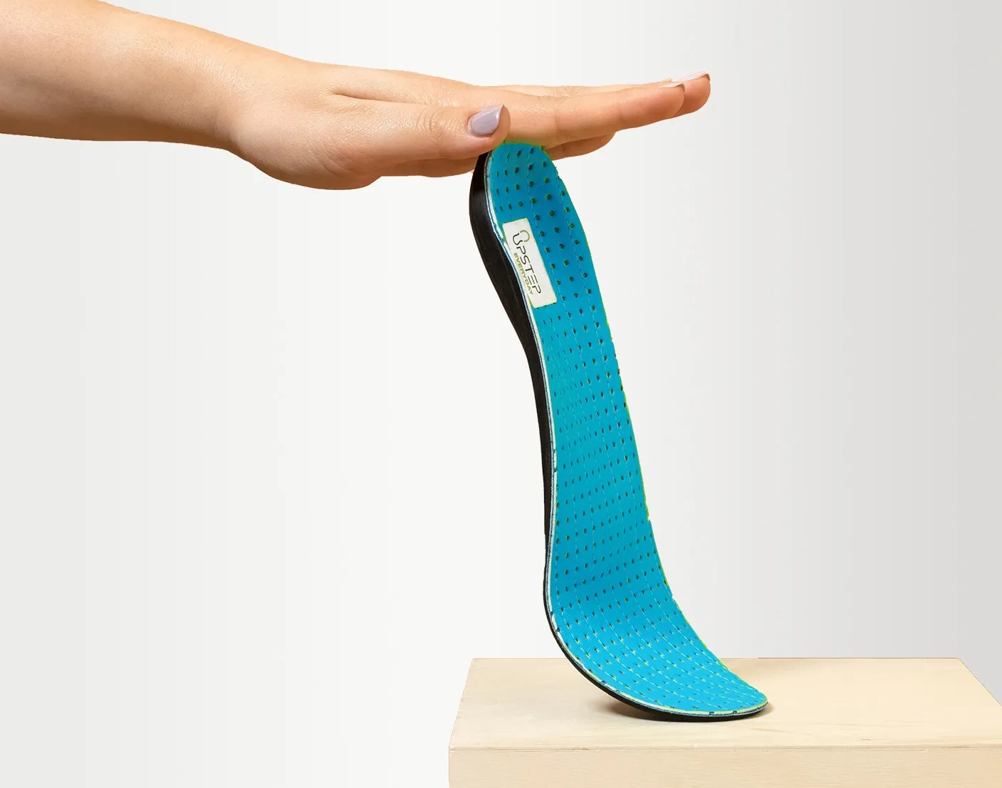 A hand holding the top of an Upstep insole for heel pain in blue to display it vertically