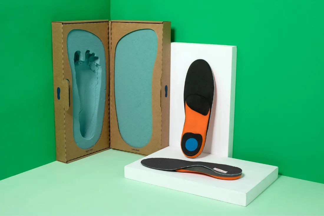 Orange and grey Upstep insoles being displayed next to a foot casting