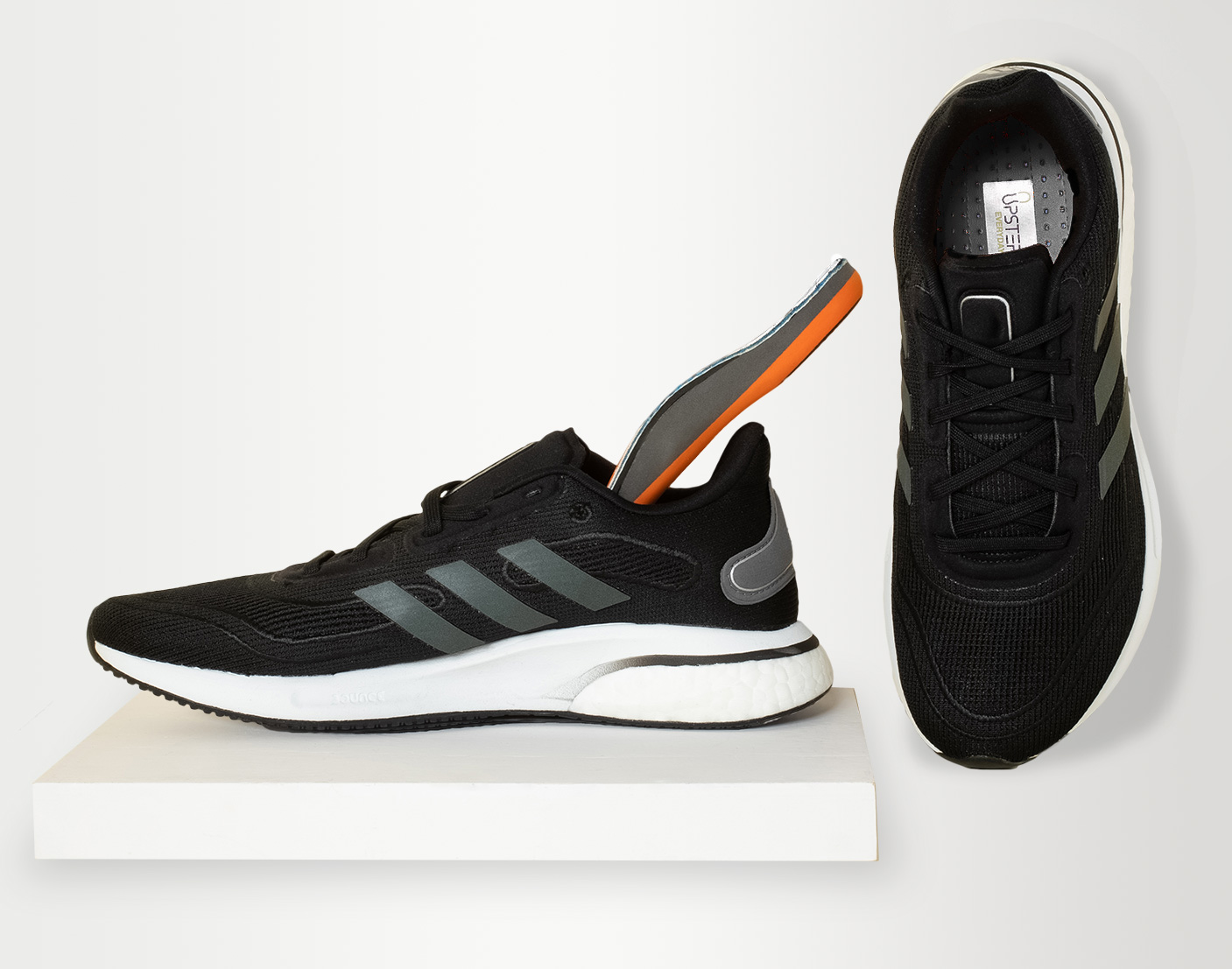 A pair of Adidas trainers with Supination Custom Orthotics made by Upstep placed inside of them.