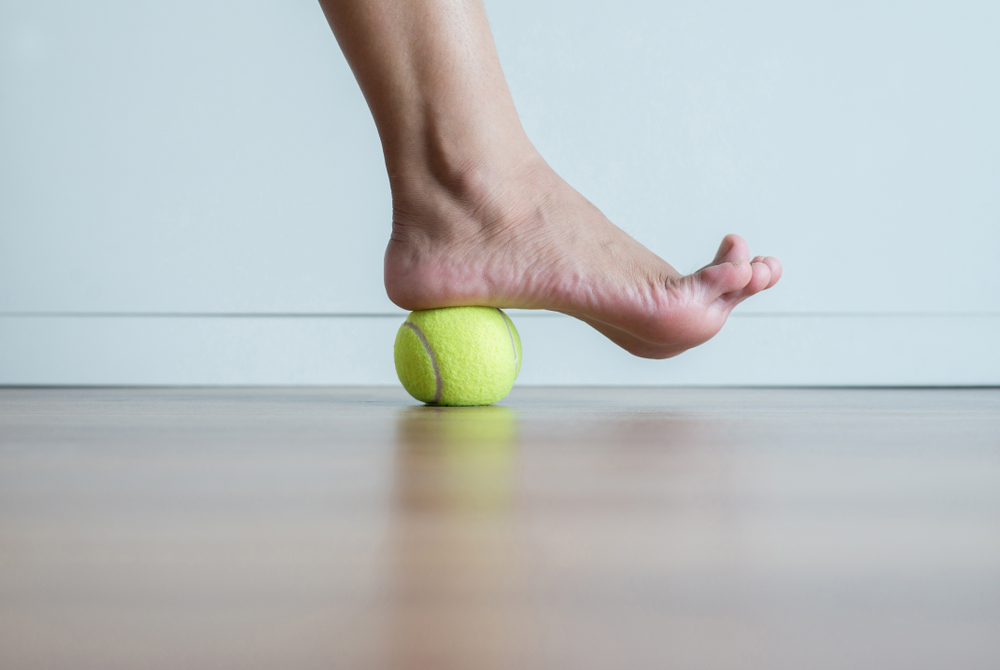 Woman rolling bare heel over tennis ball