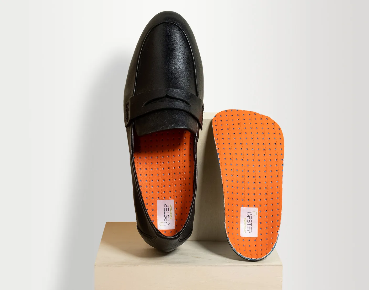 Upstep custom orthotic in orange being presented in a dress shoe with another orthotic next to it