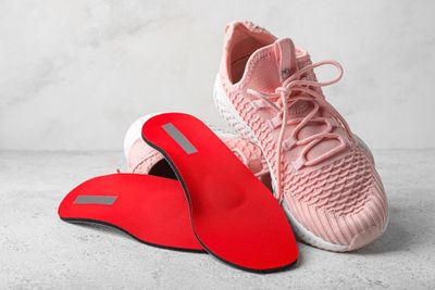 A pair of pink tennis trainers and red insoles staked up next to each other.