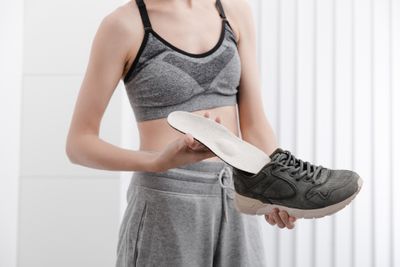 Woman in exercise clothes fitting orthopedic insole into exercise shoe