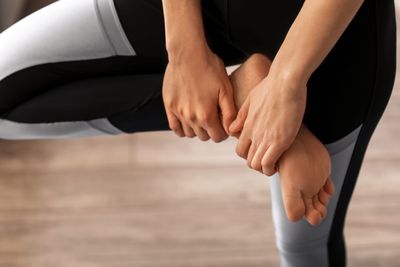 Sporty person in tights holding foot and stretching ankle while standing