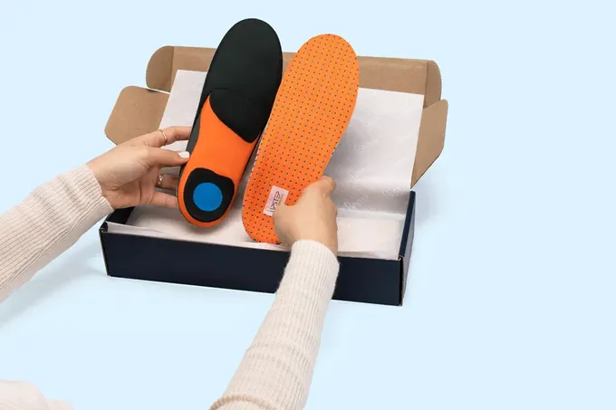 a pair of orange and black shoes insoles, custom made orthotics by Upstep in a box
