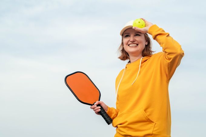 A woman holding a pickleball paddle and wearing a hat accessory.