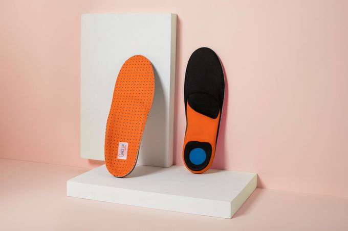 A pair of orange insoles leaning against a wall showcasing the front and back of the insoles