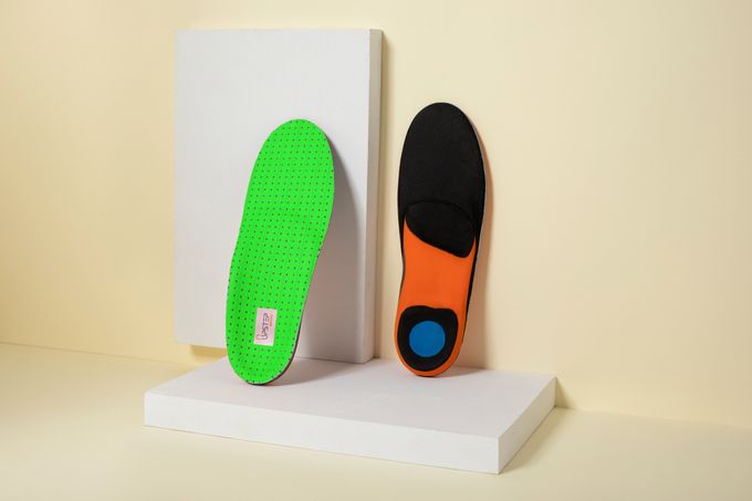 Two insoles leaning against a wall showcasing the front and back of the insoles
