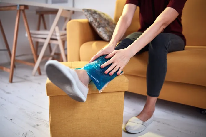 A woman sitting on a sofa and applying a cold pack onto her shin