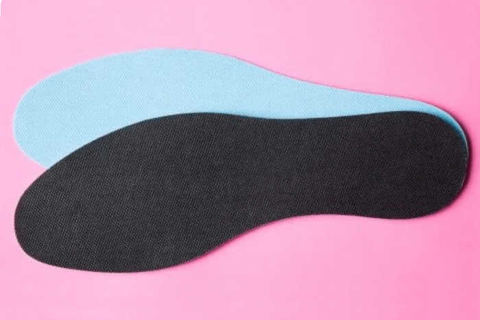 Two orthotics in black and light blue displayed on a pink background