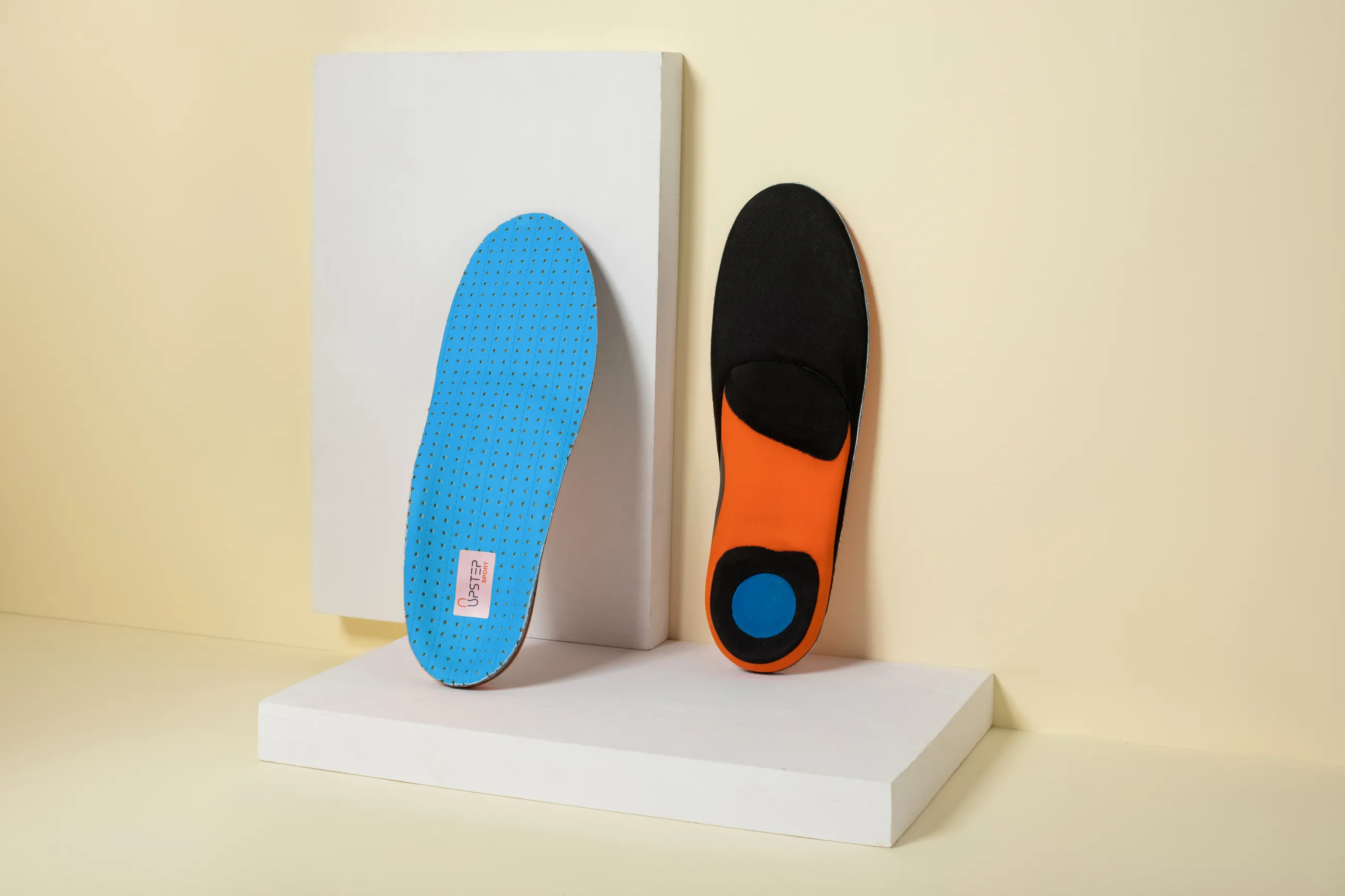 Two Upstep custom shoe insoles in blue leaned on a wall behind them, one seen from the front side, the other one from the back