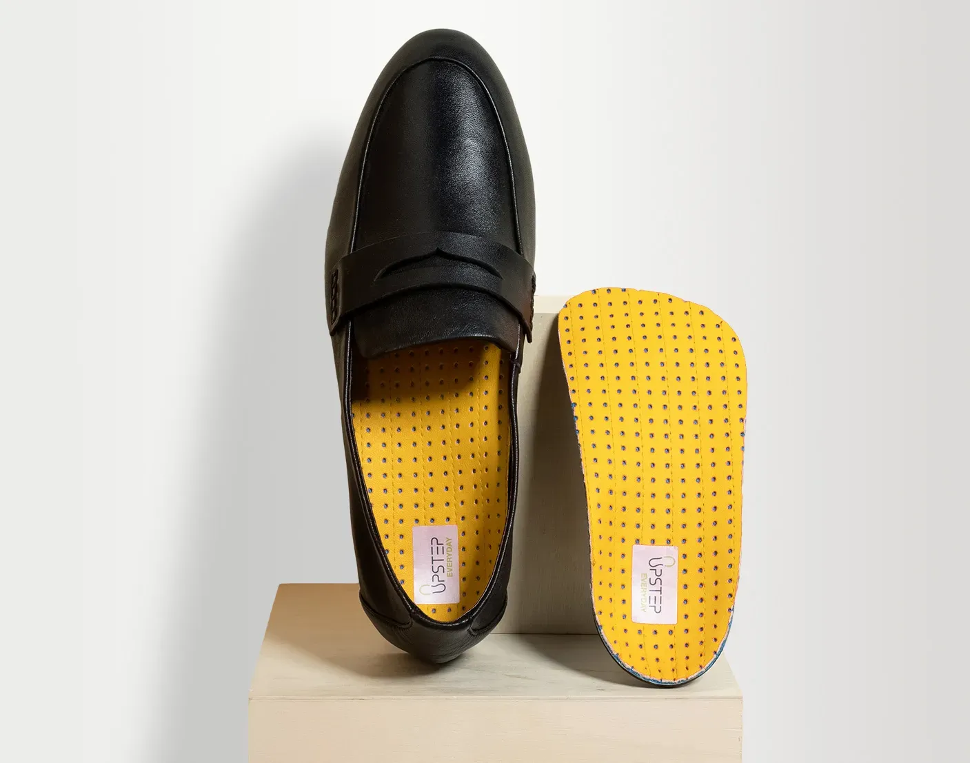 Yellow upstep custom orthotics for overpronation presented in a black formal shoe
